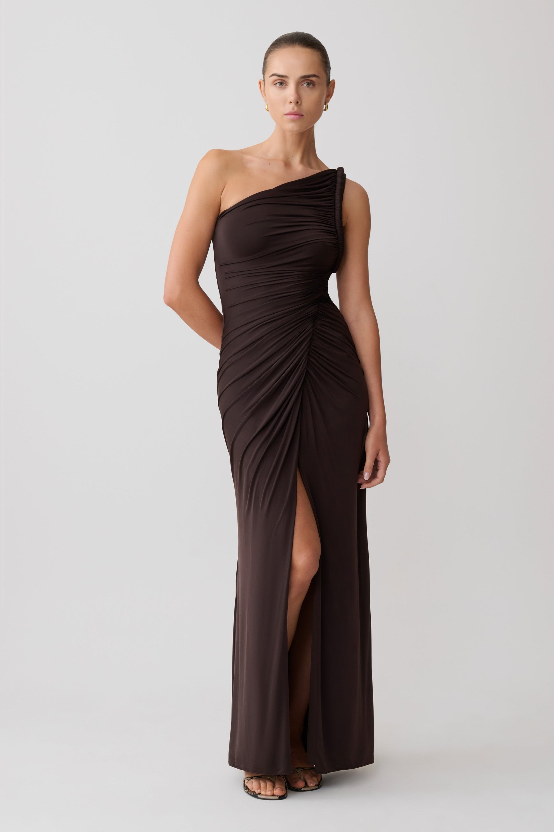 Woman wearing a brown one-shoulder maxi dress with a slit.