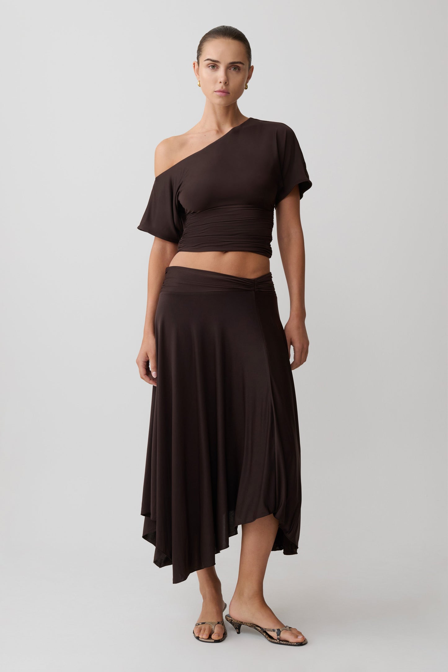 Woman wearing a brown one-shoulder top with a matching midi skirt.