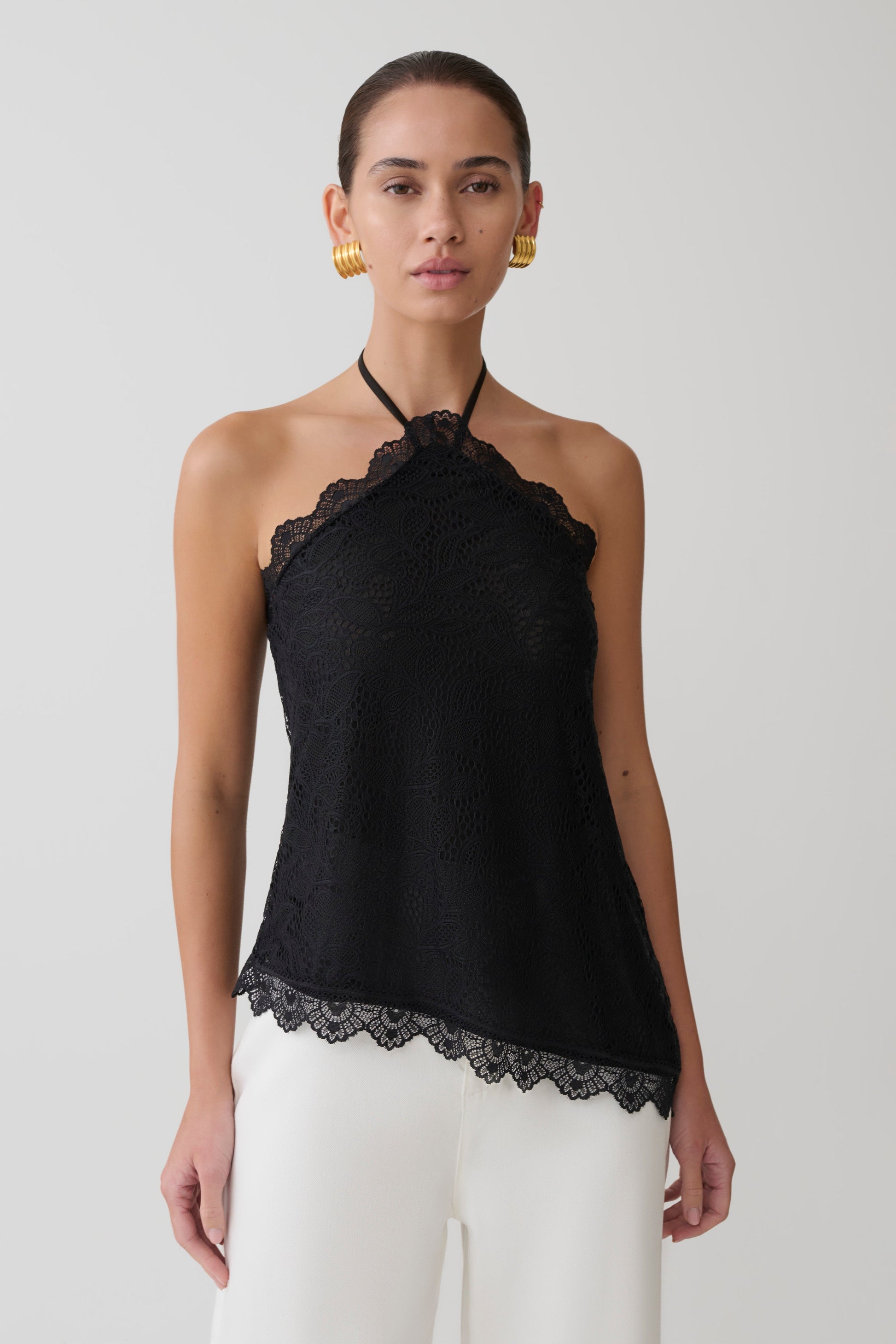 Woman wearing a black halter top with lace details on a plain background