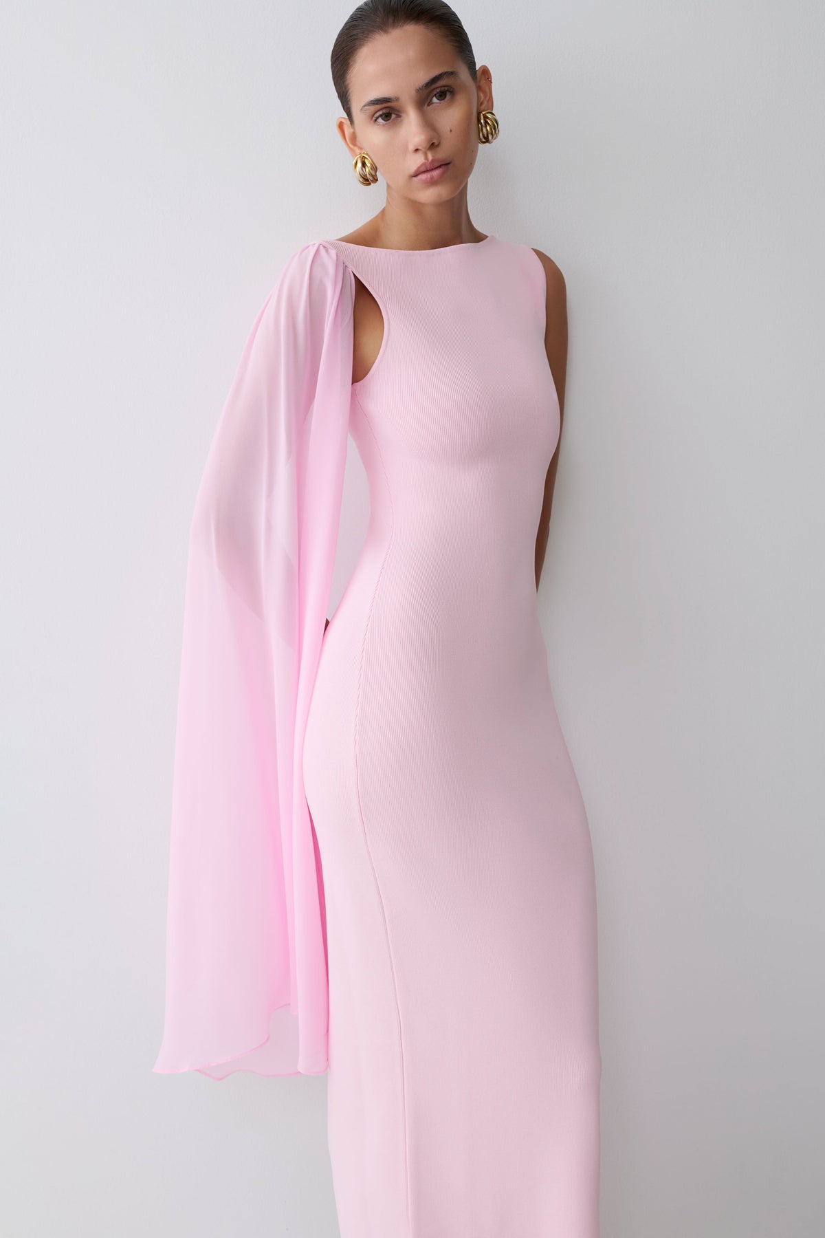 Woman wearing a pink gown with a sheer scarf overlay.