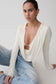 Woman wearing a white long-sleeve top and blue jeans against a plain background