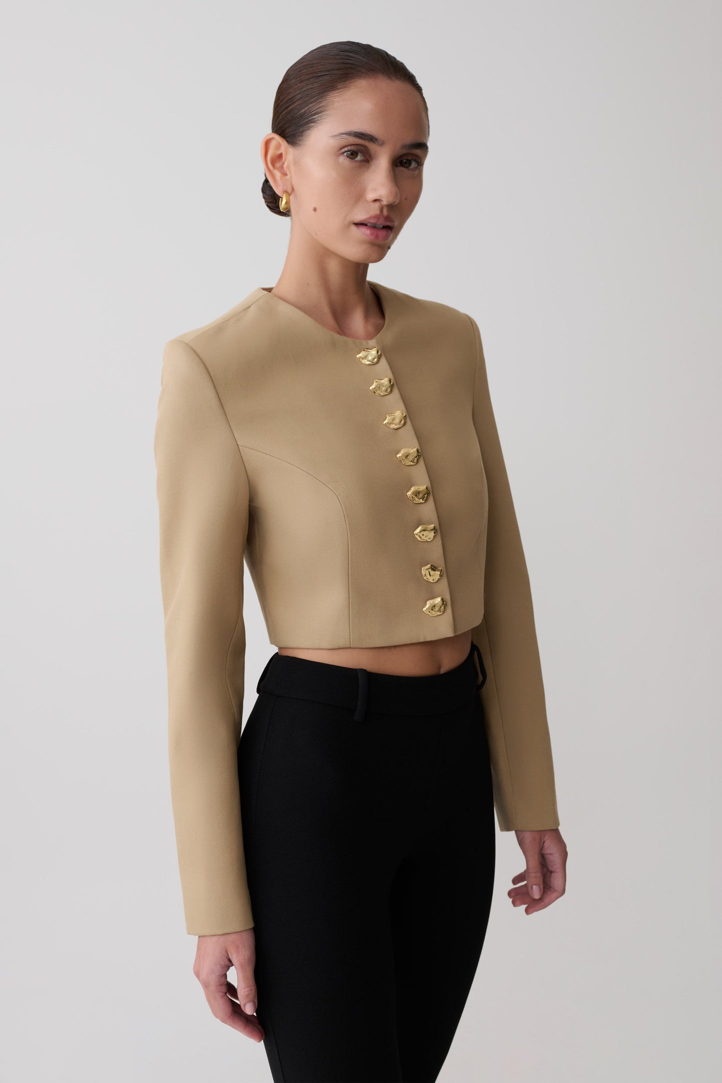 Woman wearing a beige cropped jacket with gold buttons.