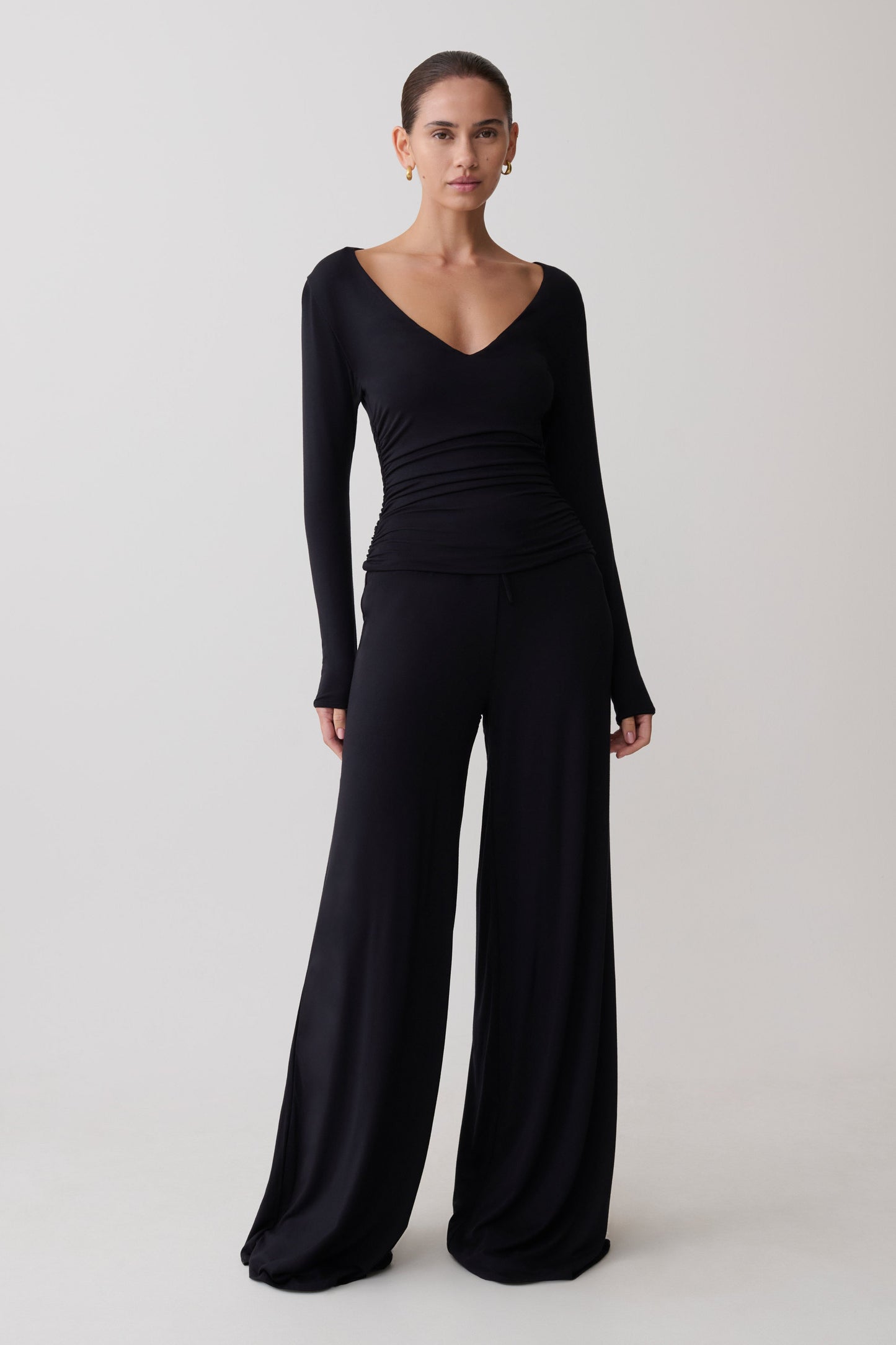 Woman wearing a black long-sleeve top and wide-leg pants on a white background