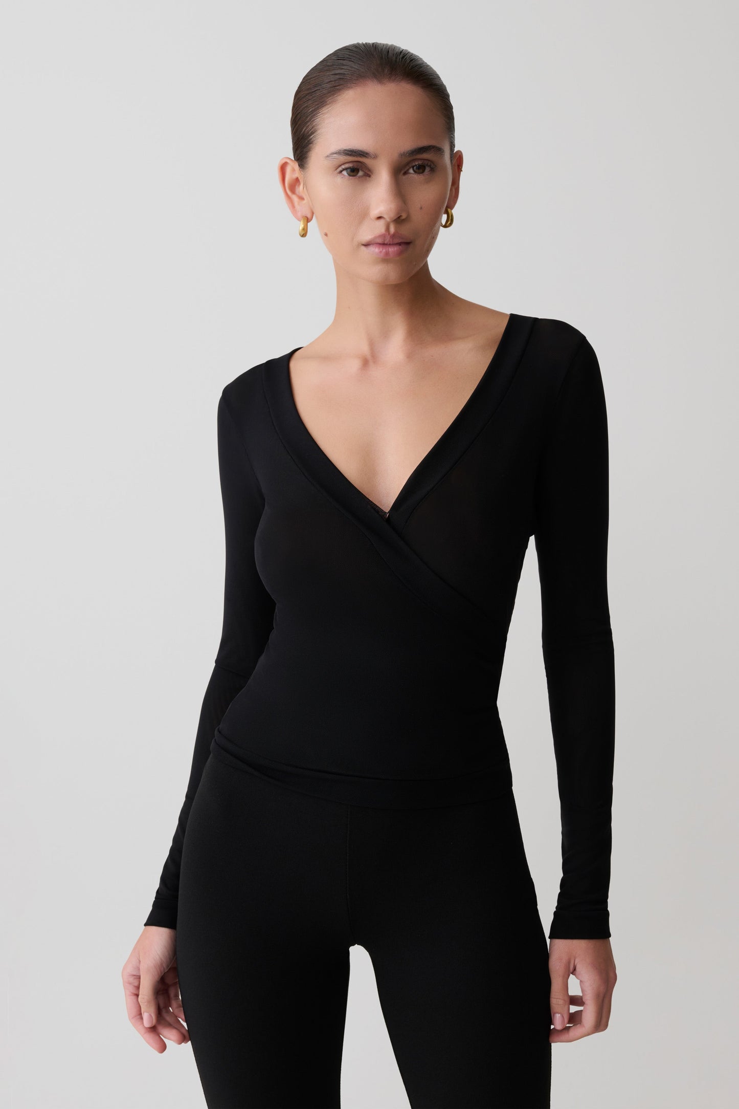 Woman wearing a black long-sleeve jumpsuit against a plain background