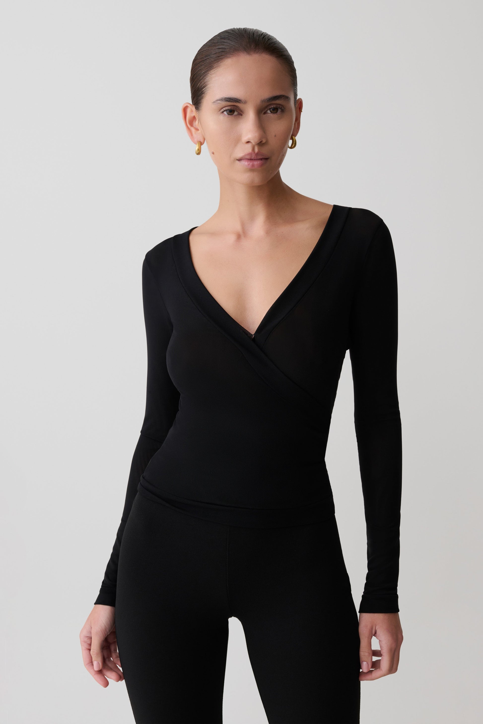Woman wearing a black long-sleeve jumpsuit against a plain background