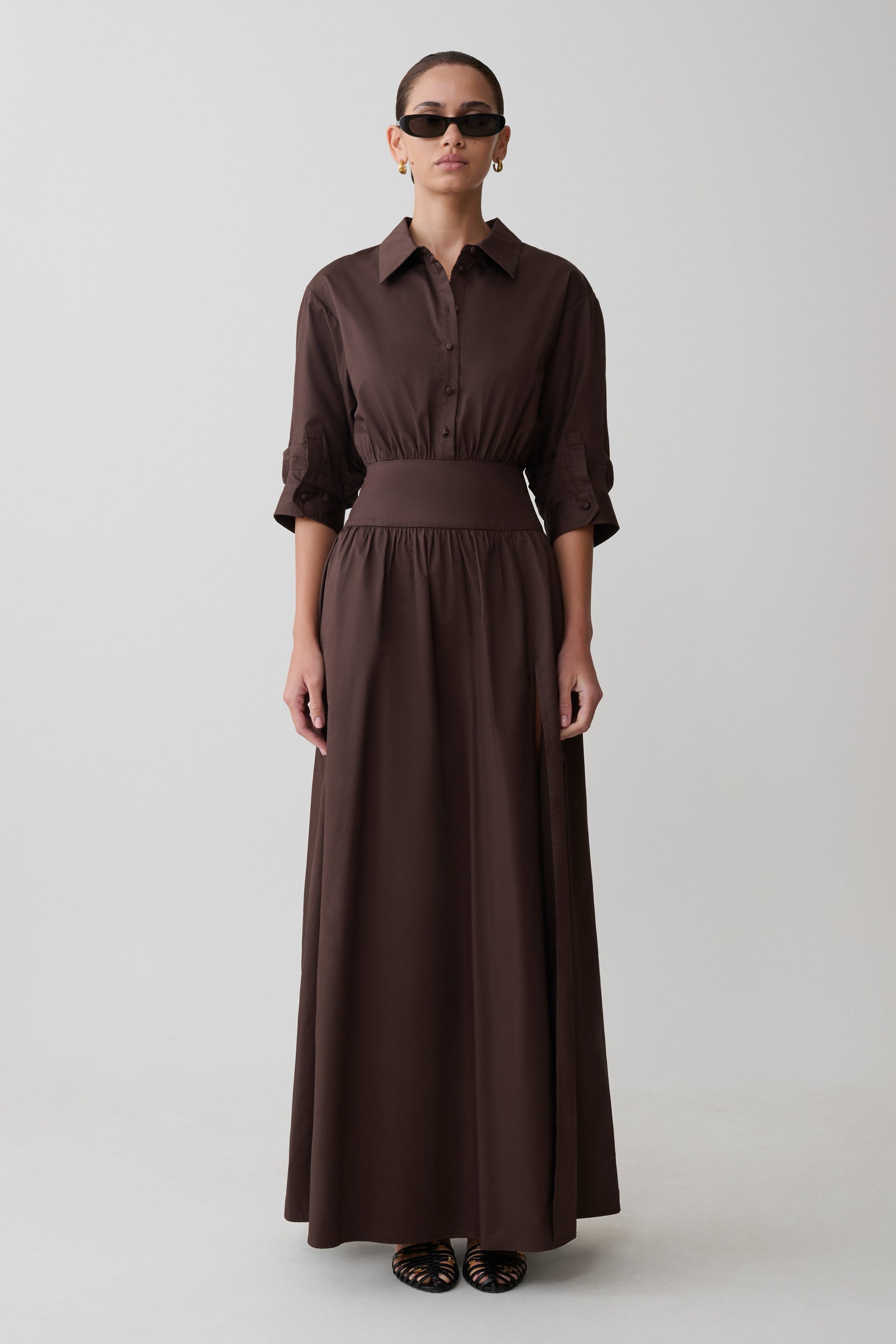 Woman wearing a long brown dress with a belt on a white background