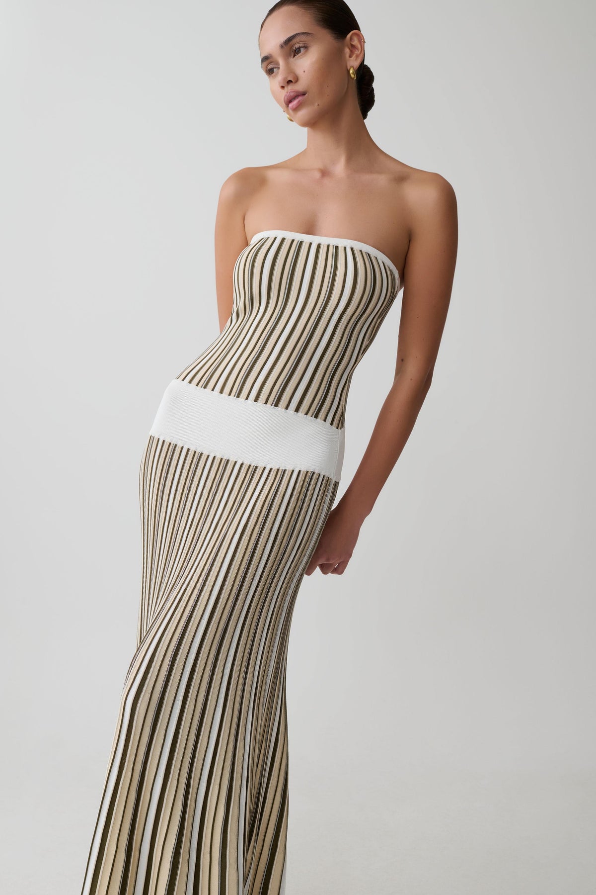 Woman wearing a strapless, long, pleated dress with a white wasitband. 