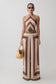 Woman wearing a patterned jumpsuit holding a straw bag on a plain background