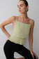 Woman wearing a light green pleated top and black pants against a plain background