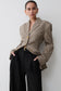 Woman wearing a brown checkered blazer and black pants against a white background