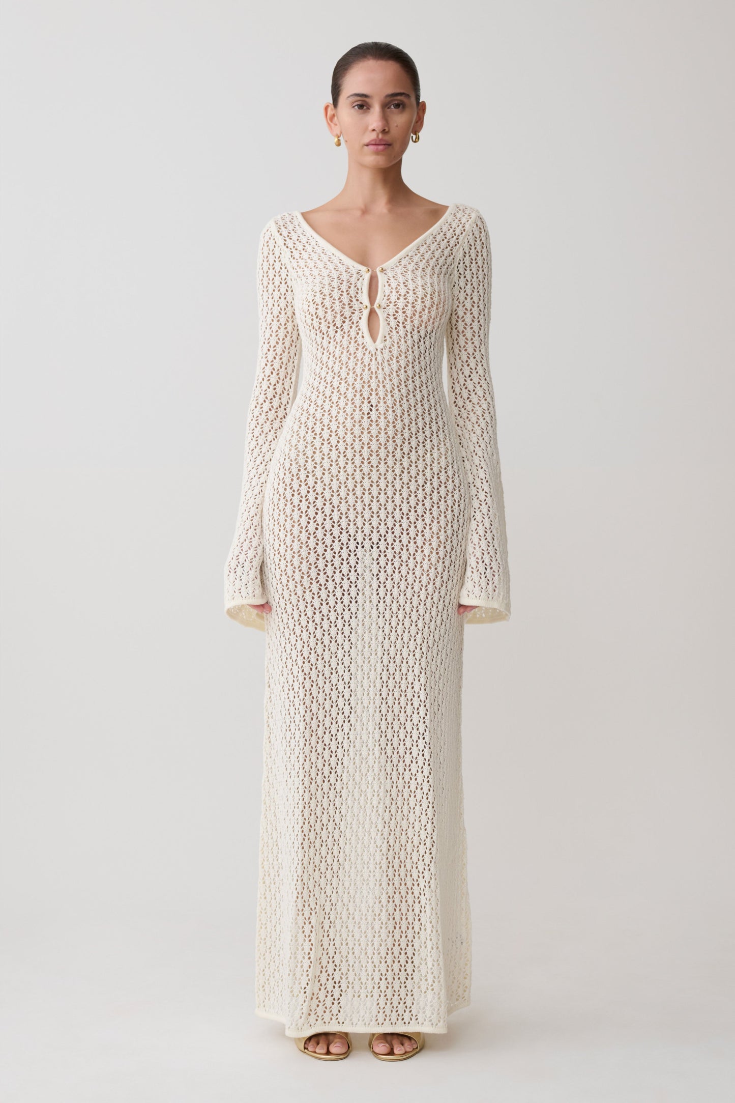 Woman wearing a long, cream-colored knitted dress against a white background