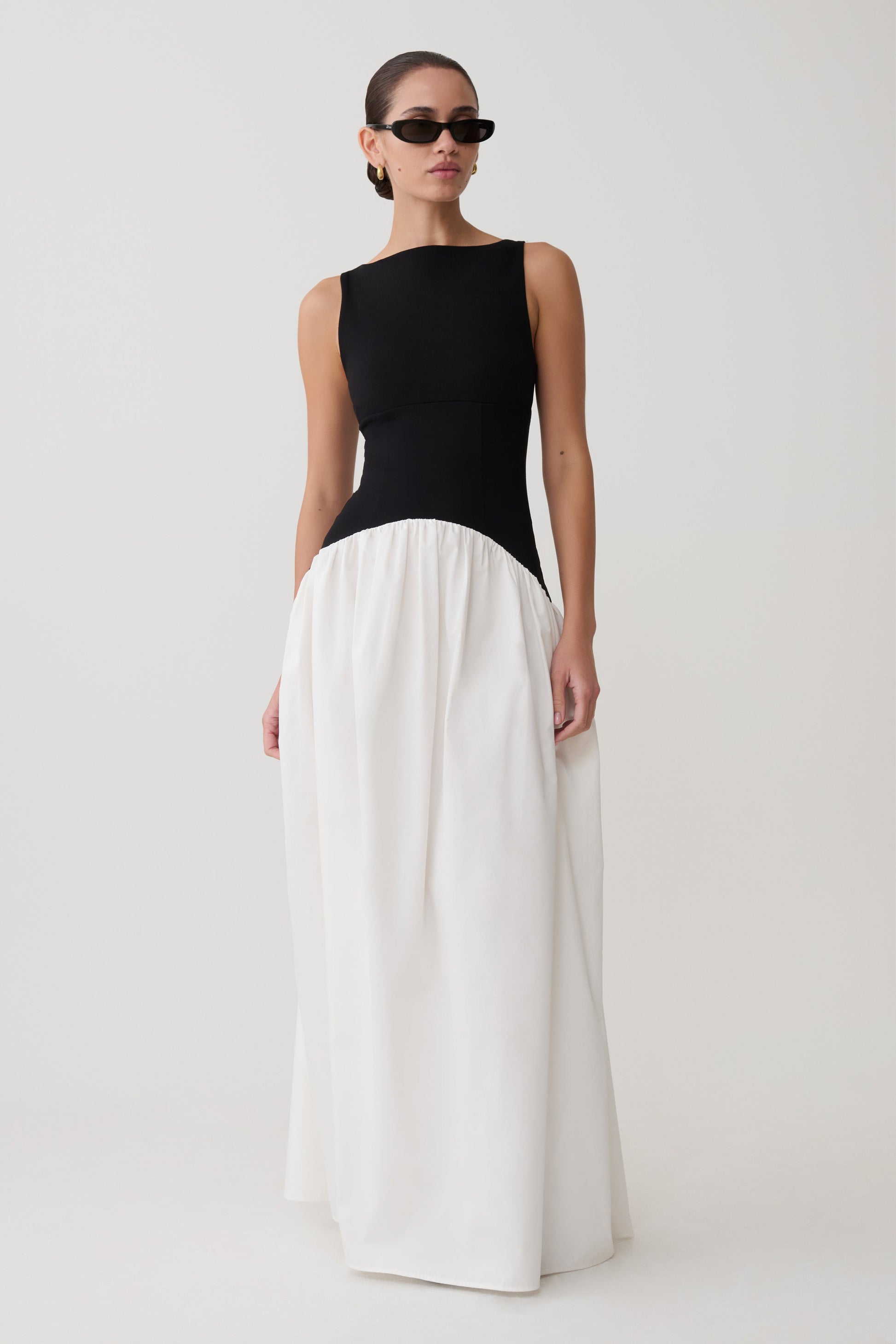 Woman wearing a black top and white pants on a plain background