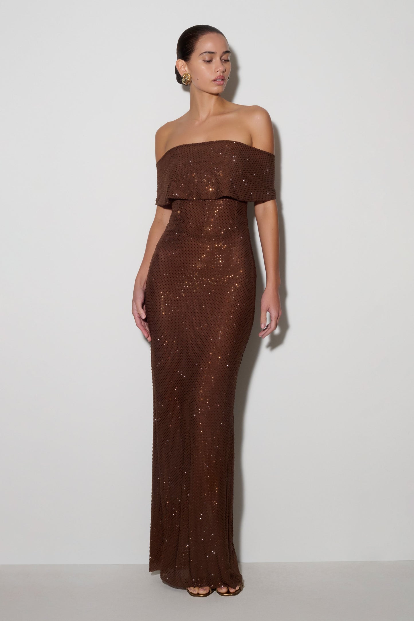 Woman wearing a brown off-shoulder evening gown against a white background