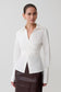Woman wearing a white blouse with a V-neckline on a plain background