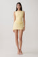 Woman wearing yellow draped mini dress.