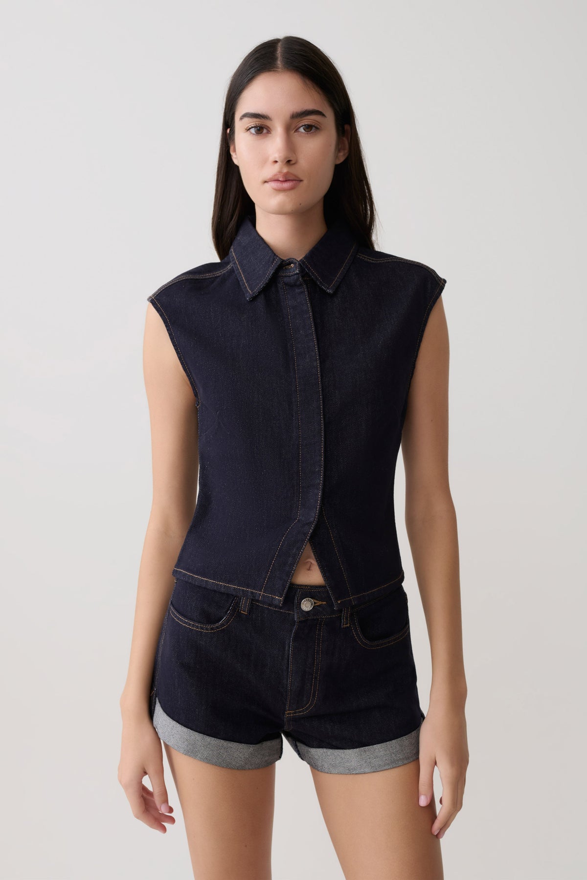Woman wearing dark blue collared denim longline top with matching denim shorts.