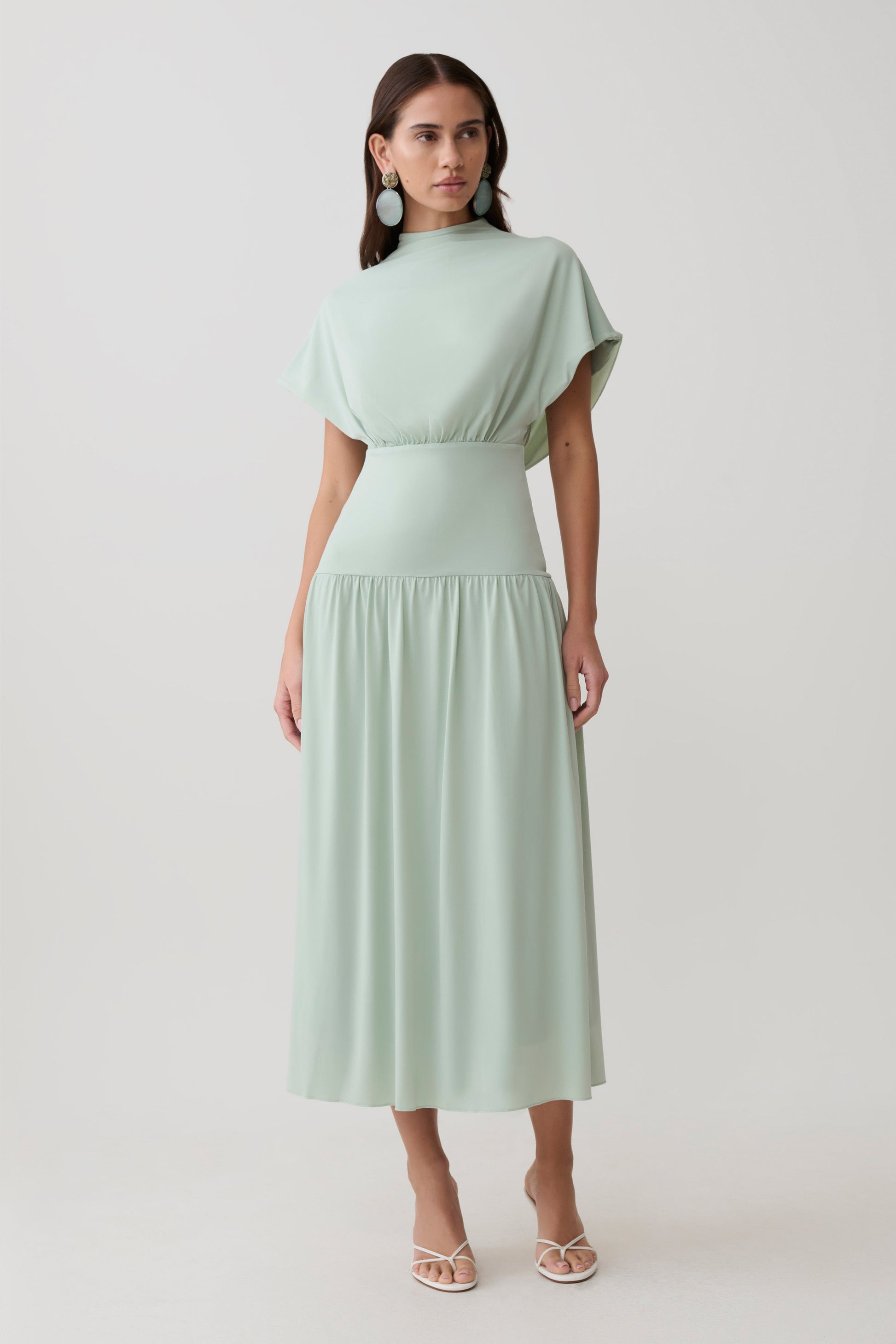 Woman wearing a light green high neck cowl midi dress.