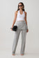 Woman wearing a white tank top and gray  wrap skirt straight leg pants.