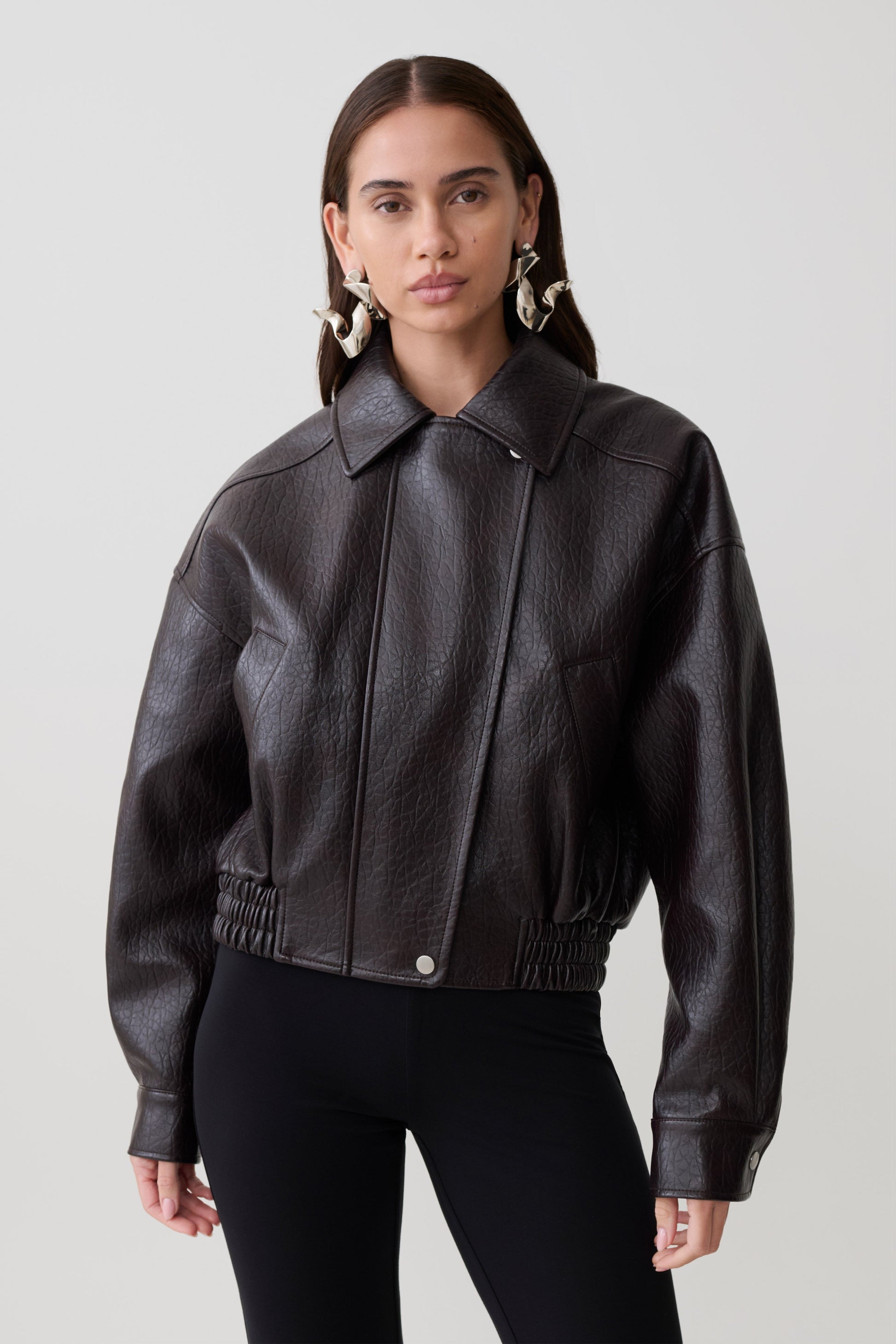 Woman wearing a brown faux leather cropped jacket.