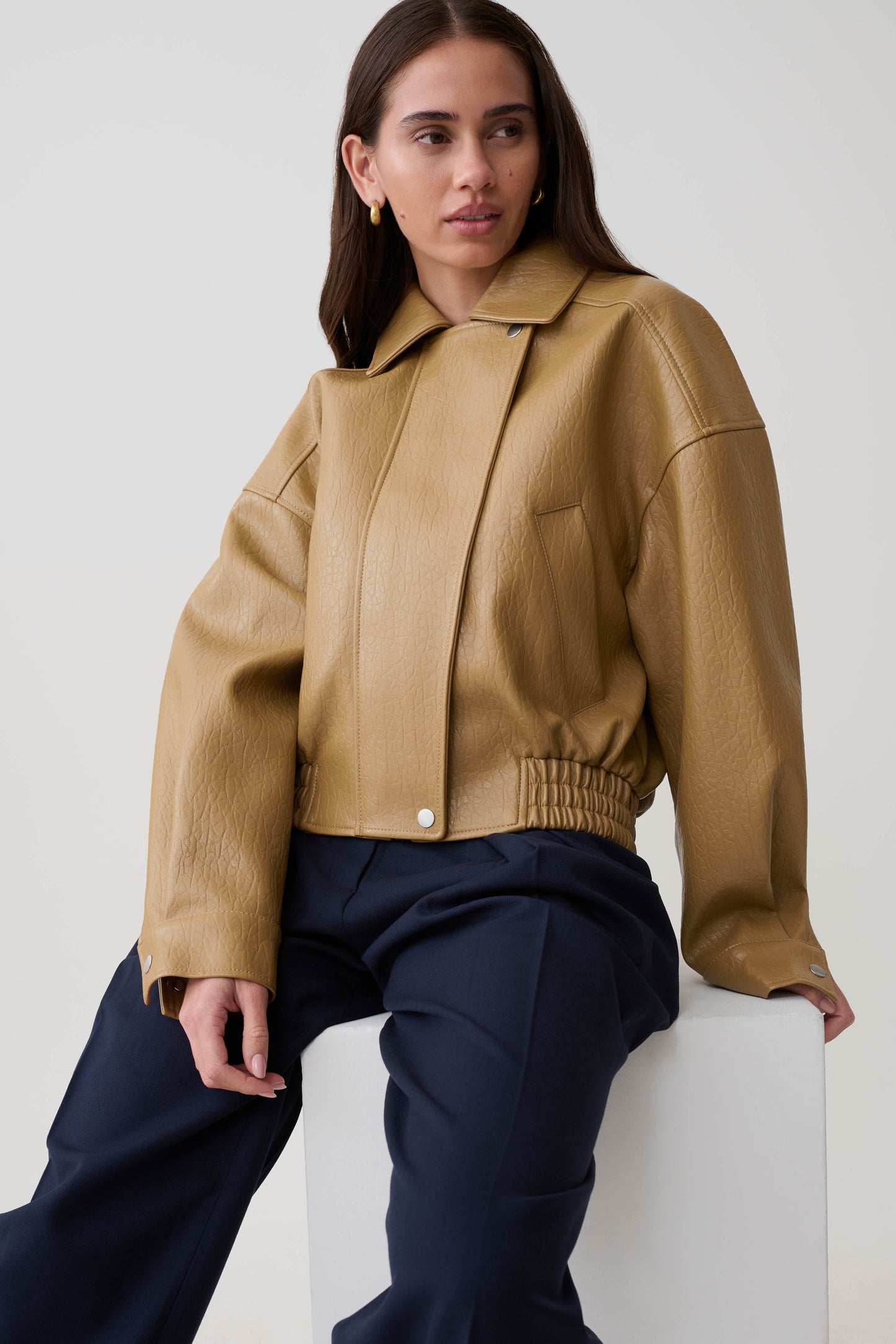 Woman wearing a tan faux leather cropped jacket.