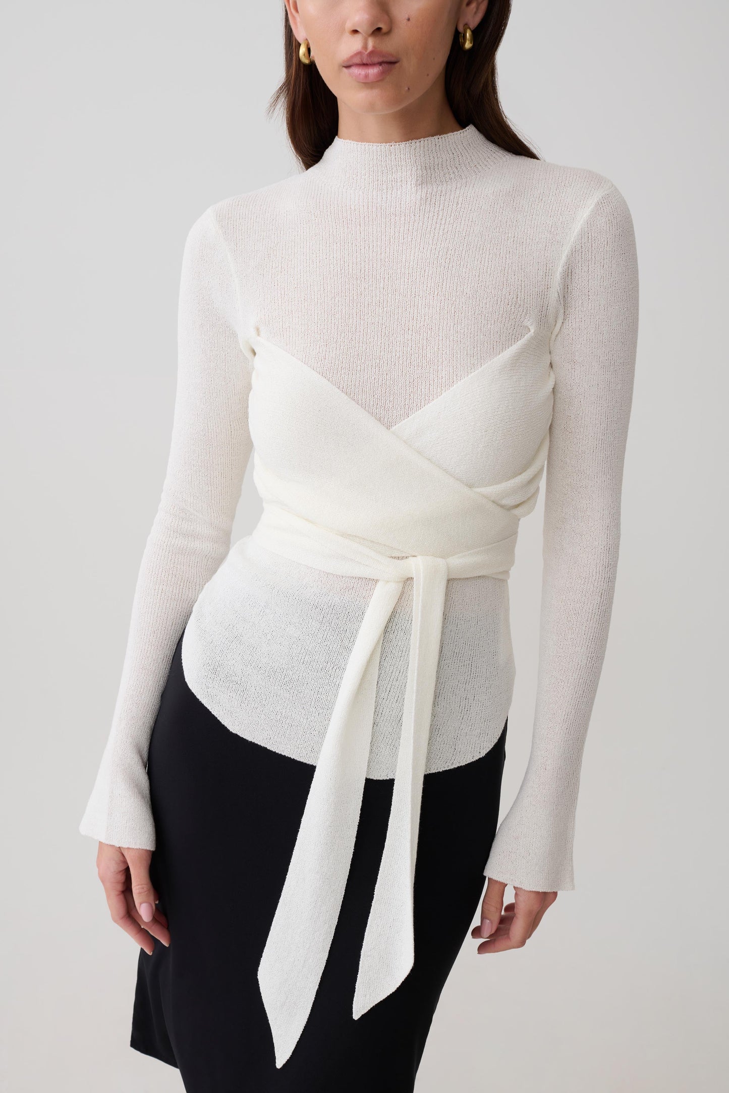 Woman wearing a white knit long-sleeve top with a tie detail.