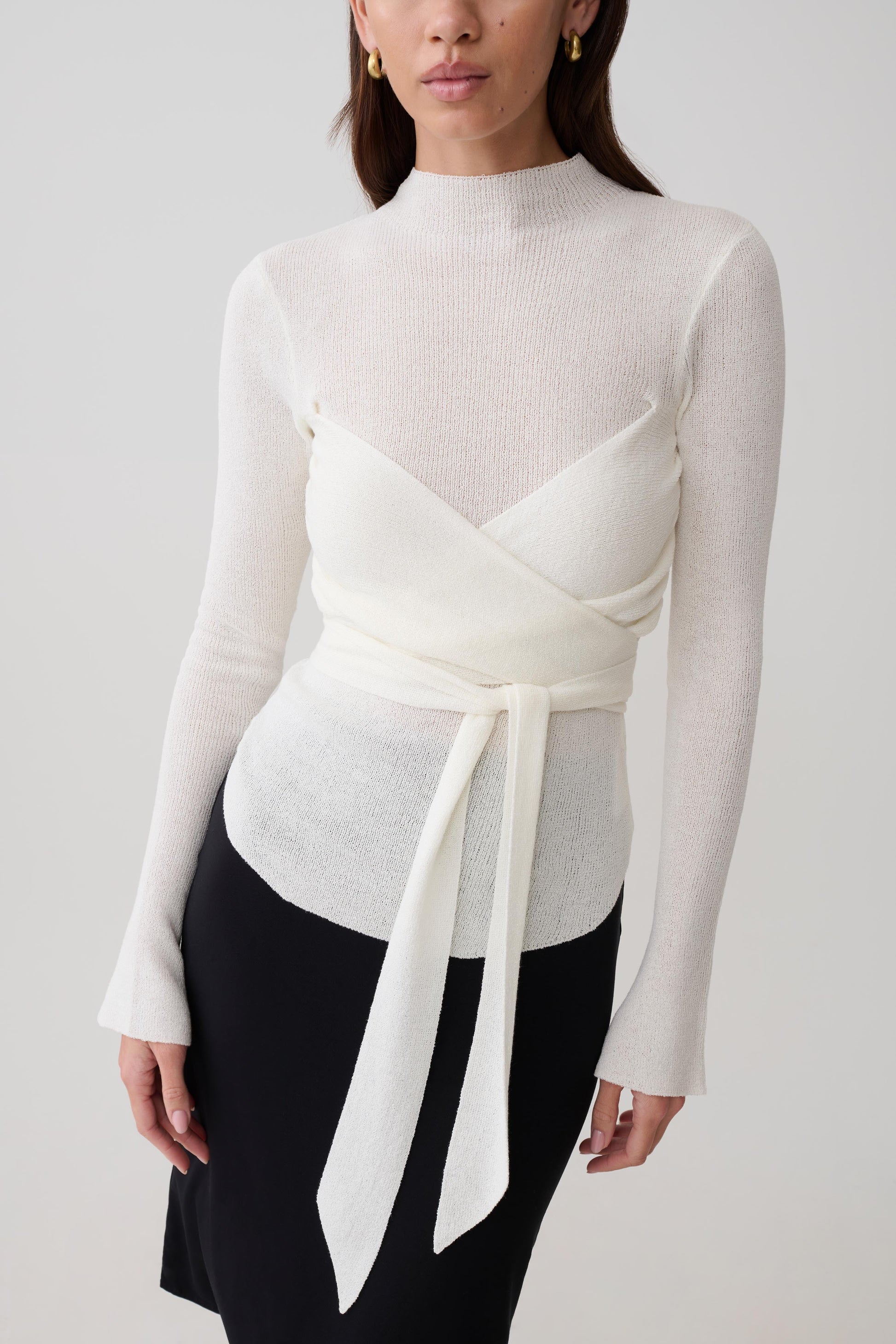 Woman wearing a white knit long-sleeve top with a tie detail.