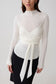 Woman wearing a white knit long-sleeve top with a tie detail.