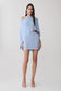 Woman wearing a light blue off-shoulder top and matching skirt.