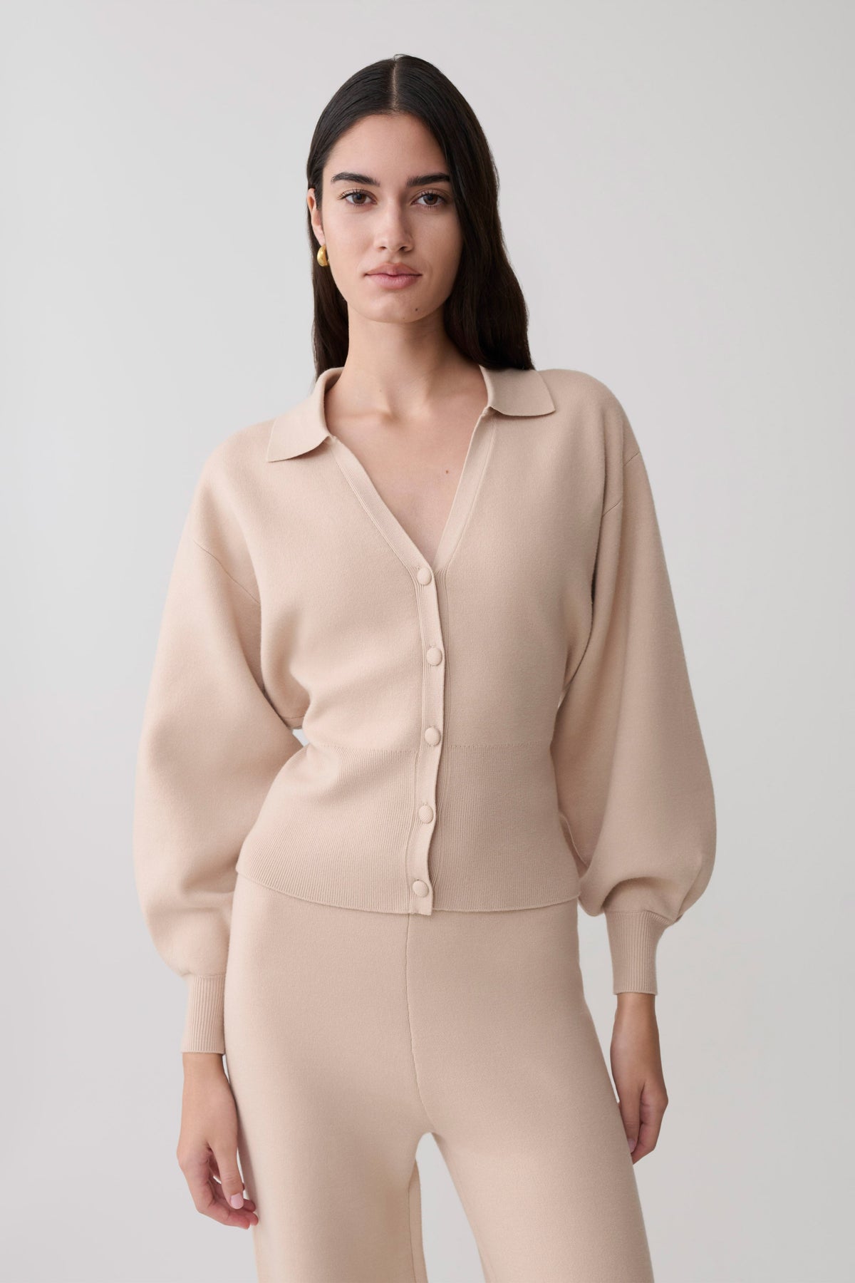 Woman wearing a beige knit blouson sleeve cardigan.