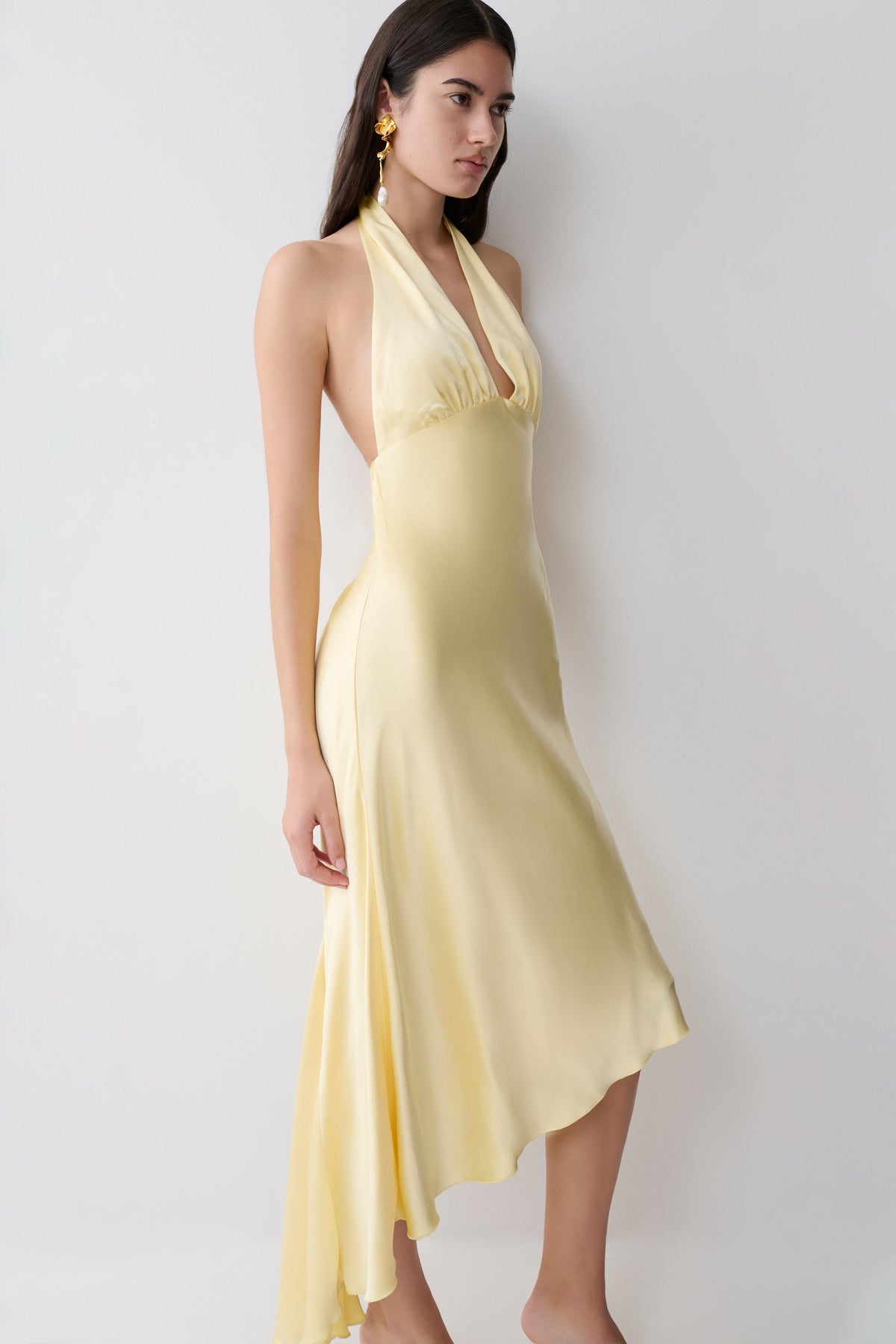 Woman wearing a yellow halter midi dress with an asymmetric hem.