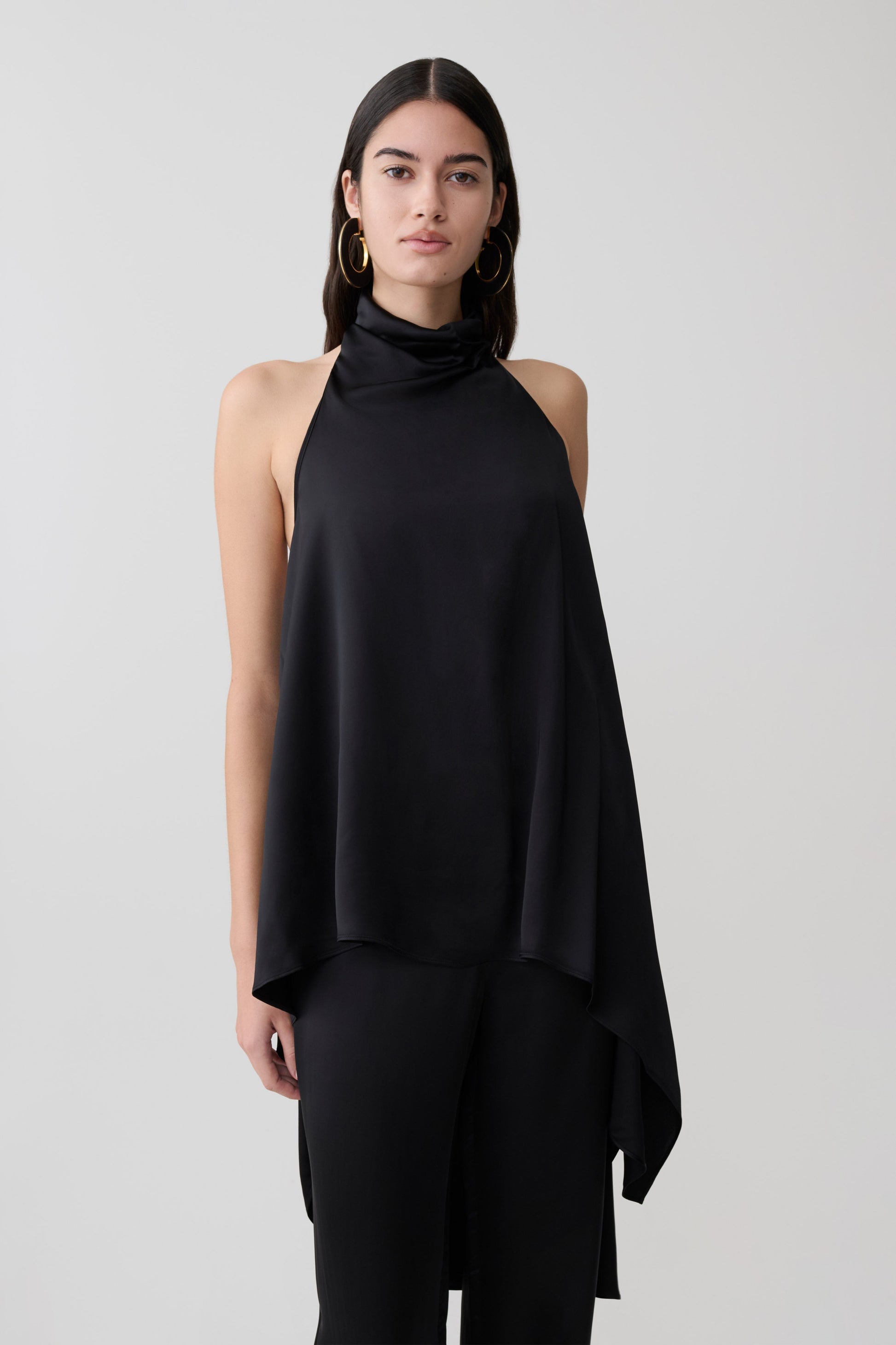 Woman wearing a black asymmetrical satin halter top.