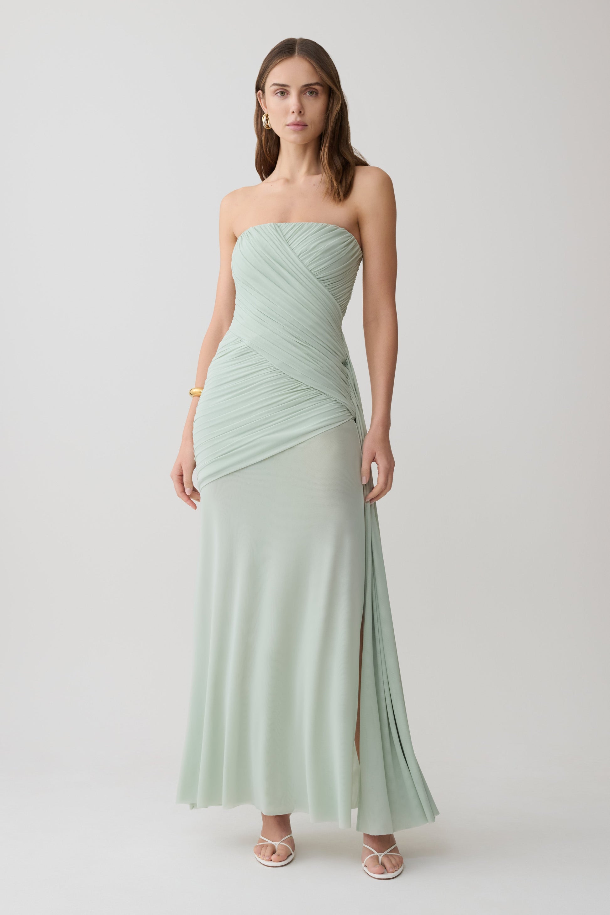 Woman wearing a light green strapless ruched mesh maxi dress.