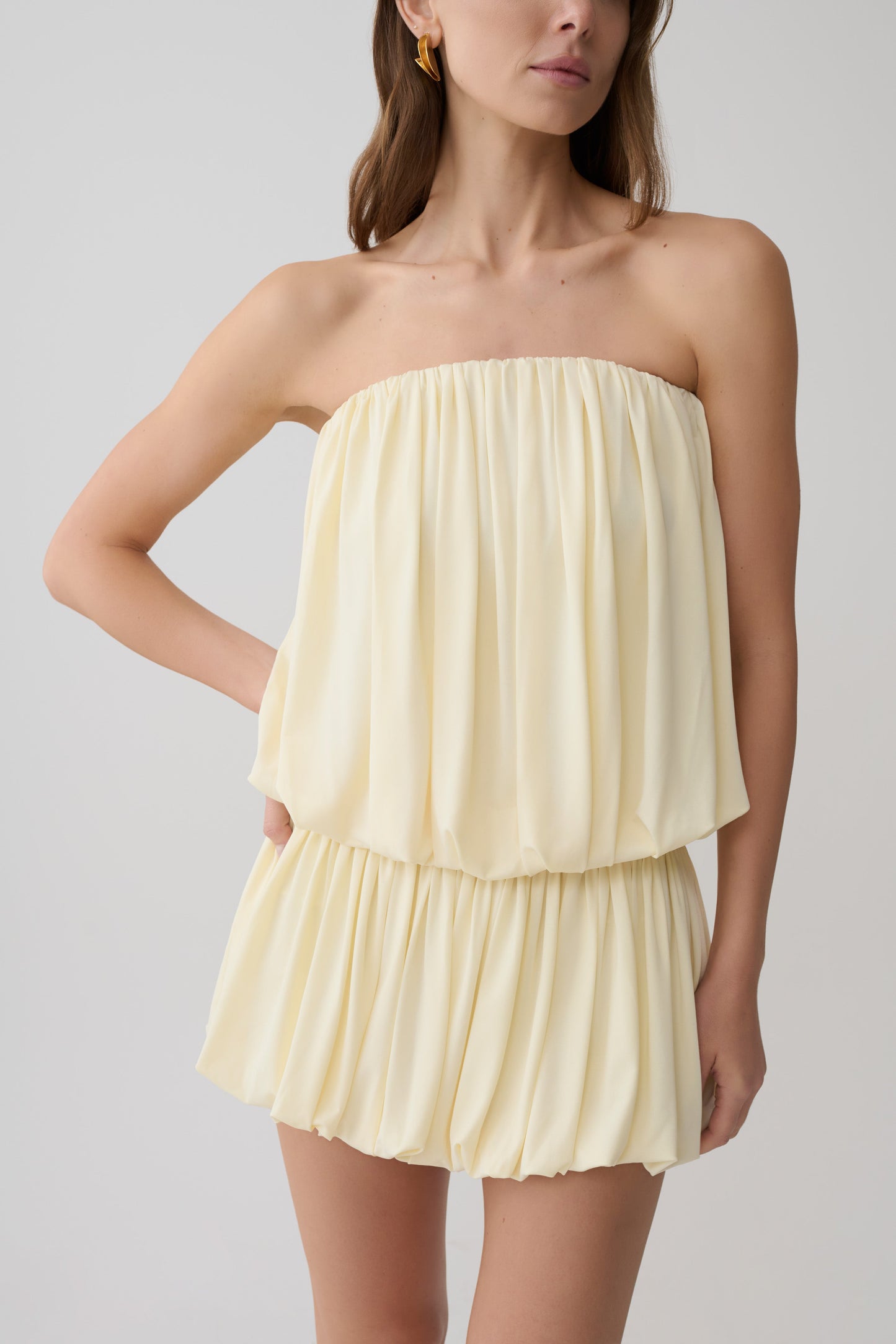 Woman wearing a light yellow strapless gathered bubble mini dress.