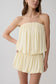 Woman wearing a light yellow strapless gathered bubble mini dress.