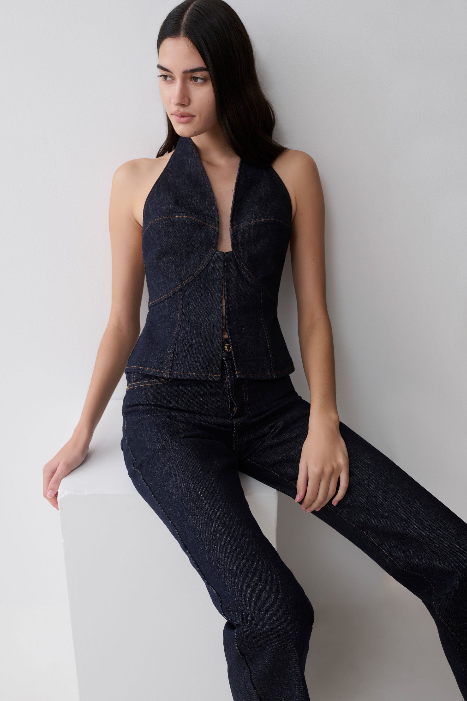 Woman wearing a dark blue halter longline denim top.