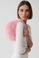 A model wearing a white ribbed long-sleeve top holds a large, round, light pink beaded bag against her shoulder, photographed against a clean light gray studio background.