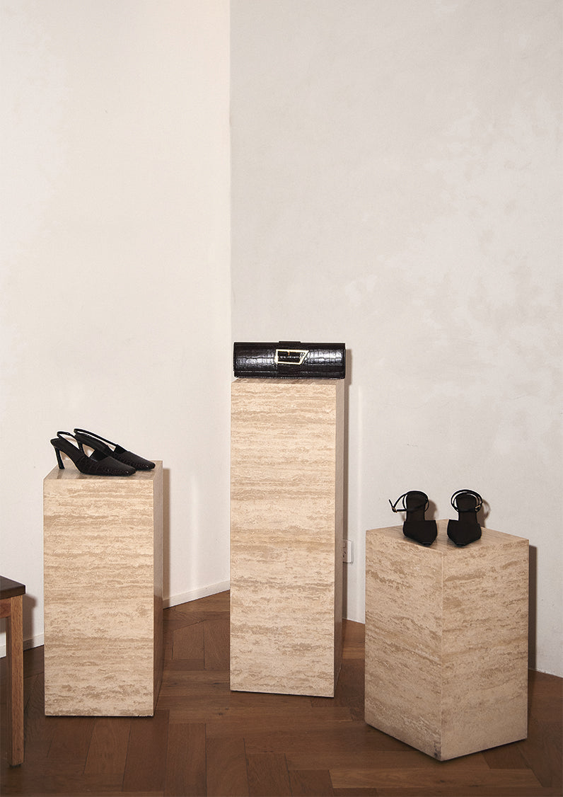 Three stone-like pedestals with shoes on a plain wall background.