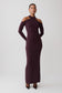 A woman modeling a long-sleeve, high-neck, bodycon maxi dress in a deep plum purple color, styled with pointed-toe heels against a light gray studio background.