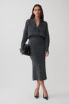A woman modeling a dark gray knit long-sleeve dress, styled with black pointed-toe heels and a black clutch bag against a light gray studio background.