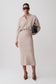 A model wearing a light beige knit long-sleeve collared midi dress, styled with dark sunglasses, a small black handbag, and brown pointed-toe heels against a light gray studio background.