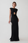 A woman modeling a floor-length black gown with a cutout at the waist and cap sleeves, holding a small white clutch against a plain light gray studio background.