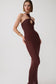 A woman modeling a fitted halter-neck bodycon dress in a deep burgundy or maroon knit, featuring a keyhole cutout at the bust. She is posed against a clean, light gray studio background.
