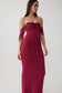A woman modeling a strapless off-the-shoulder maxi dress in deep burgundy. The dress features a ruched bodice and sheer mesh sleeves, shown against a plain light gray studio background.
