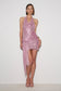A model wearing a pink sequined halter mini dress with a draped wrap-style skirt and high slit, paired with clear high-heeled sandals, against a plain white studio background.