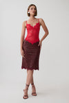 A model wearing a two-piece lace set consisting of a bright red lace camisole top and a dark burgundy lace midi skirt, paired with strappy high-heeled sandals against a light gray studio background.