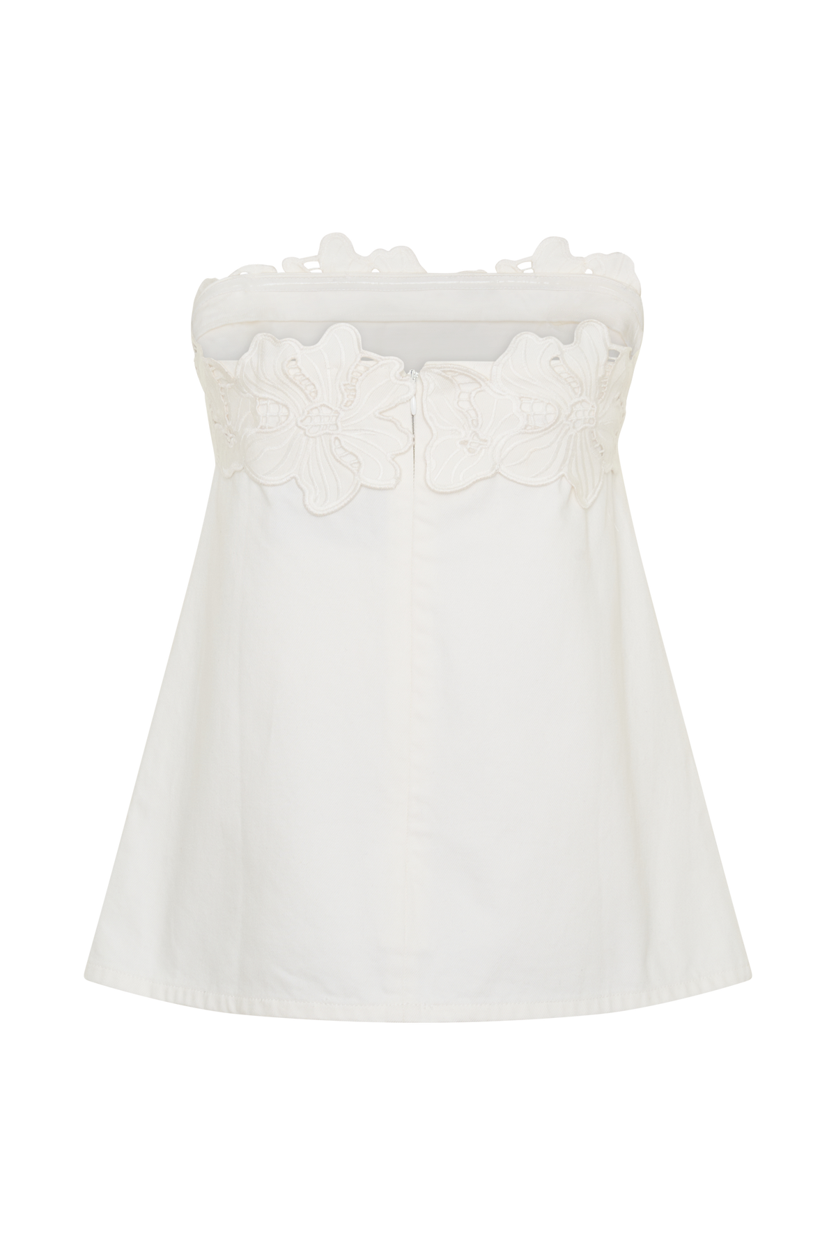 A woman modeling a strapless white top with a decorative floral lace trim across the bust, paired with wide-leg blue jeans, against a plain light gray studio background.