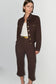 A model wearing a dark brown cropped jacket and matching cropped trousers with gold-tone buttons and a gold belt, styled over a white top against a light gray studio background.