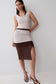A woman modeling a sleeveless bodycon dress with a light blush pink upper section and a sheer dark brown lower skirt, paired with black strappy heels against a plain light gray studio background.