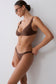 A woman modeling a solid brown two-piece bikini set against a plain light gray wall. She is wearing dark brown sunglasses and has her hair tied back in a bun.