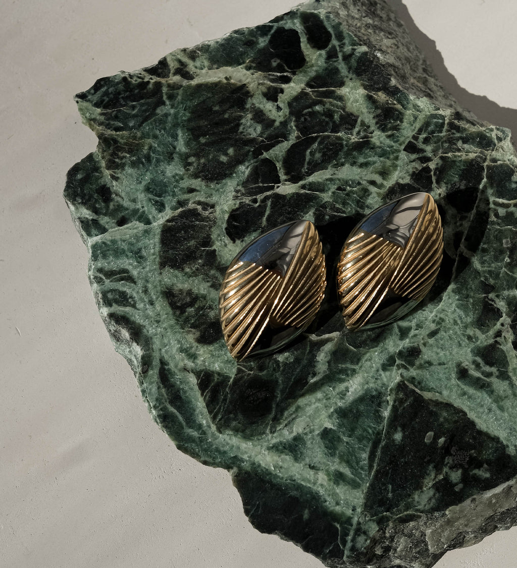 Pair of gold earrings on a green stone surface.